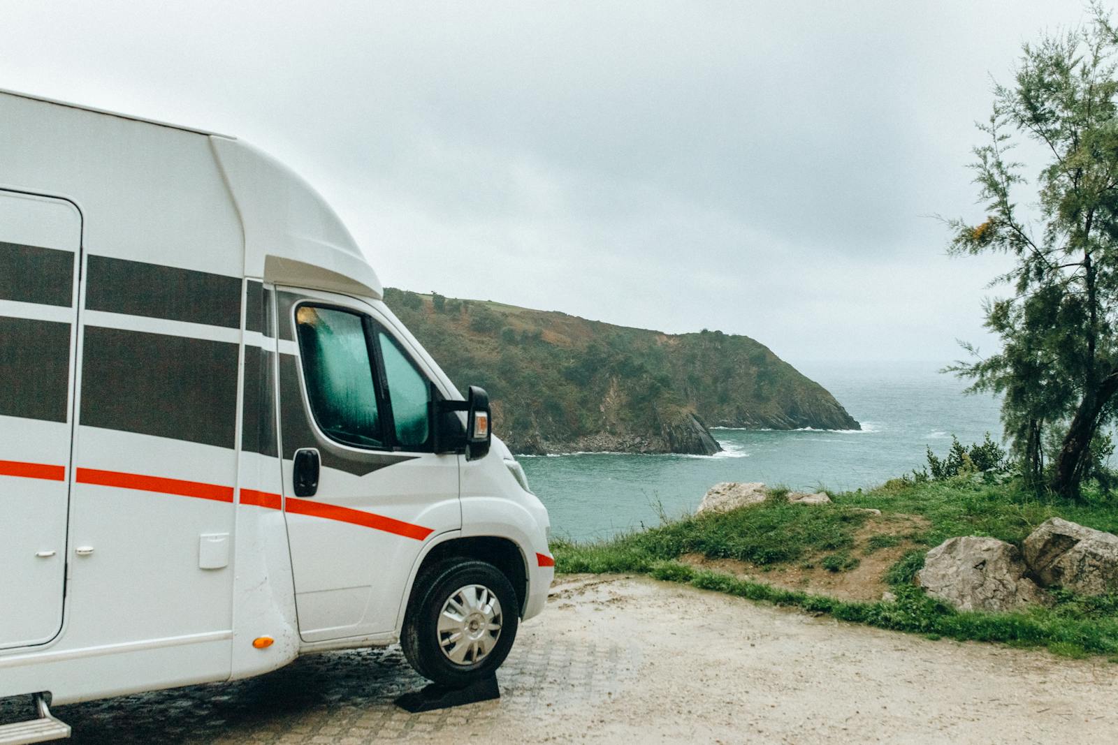 recreational vehicle, scenic view of a camper van parked by the ocean cliffs on a cloudy day.